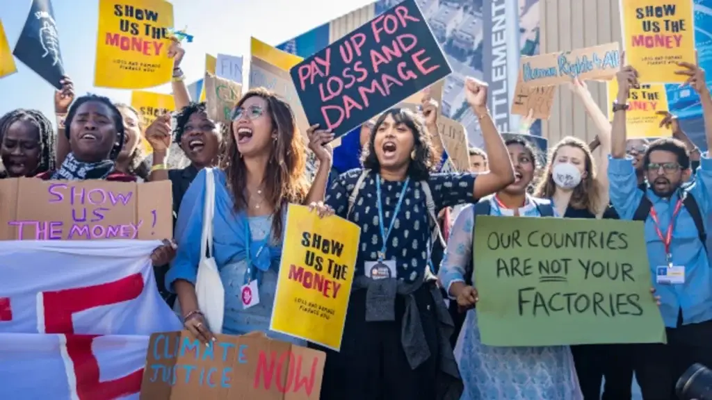 Group of climate activists holding protest signs demanding climate justice and financial reparations.