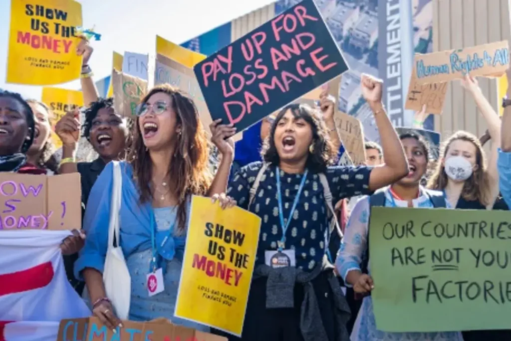 Group of climate activists holding protest signs demanding climate justice and financial reparations.