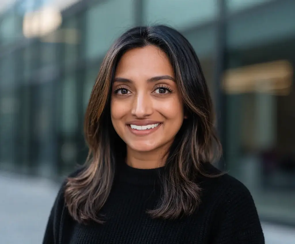 Smiling woman in a black sweater outdoors, with a blurred background of a glass building.