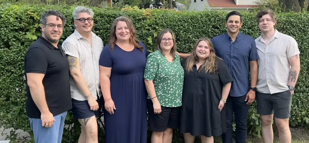 A group of people standing together in front of a green hedge, smiling for the camera.
