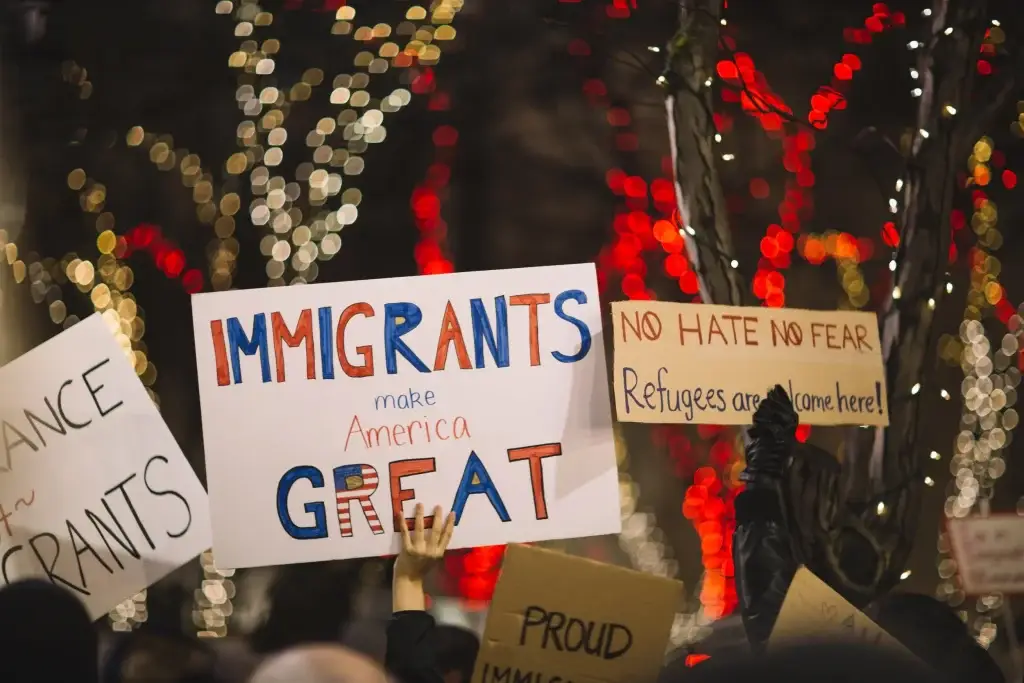 Protest signs advocating for immigrant rights with festive lights in the background.