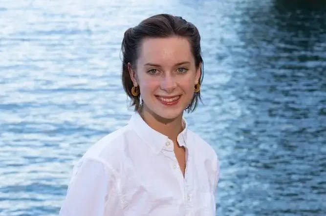 Smiling woman in a white shirt standing by a body of water.