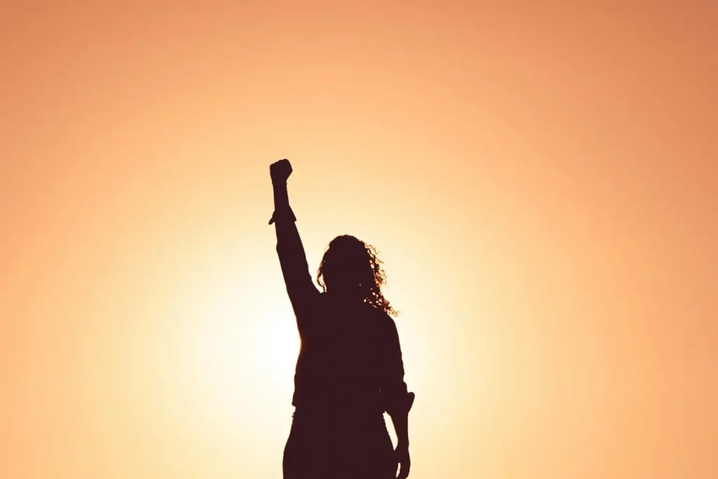 Silhouette of person raising fist against a vibrant sunset, symbolizing empowerment and triumph.