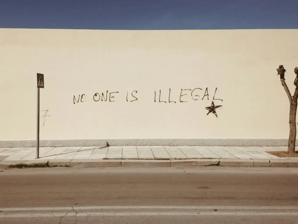 Graffiti on a wall reading No One Is Illegal with a star symbol, promoting social justice and equality.