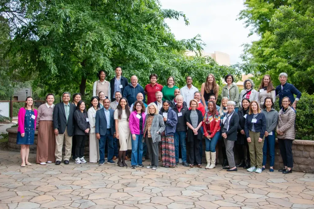 Large group of diverse people posing together outdoors on a stone walkway with trees in the background.