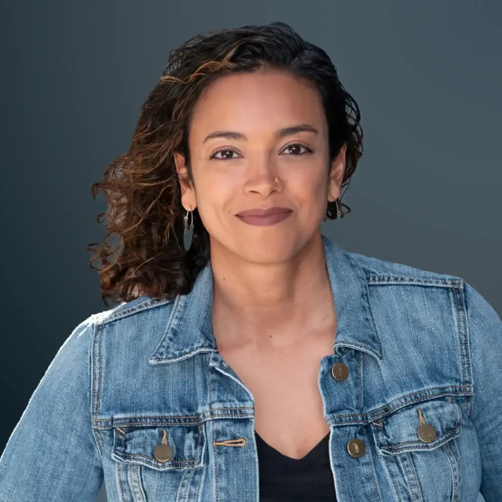 Person in denim jacket smiling confidently with a neutral background.