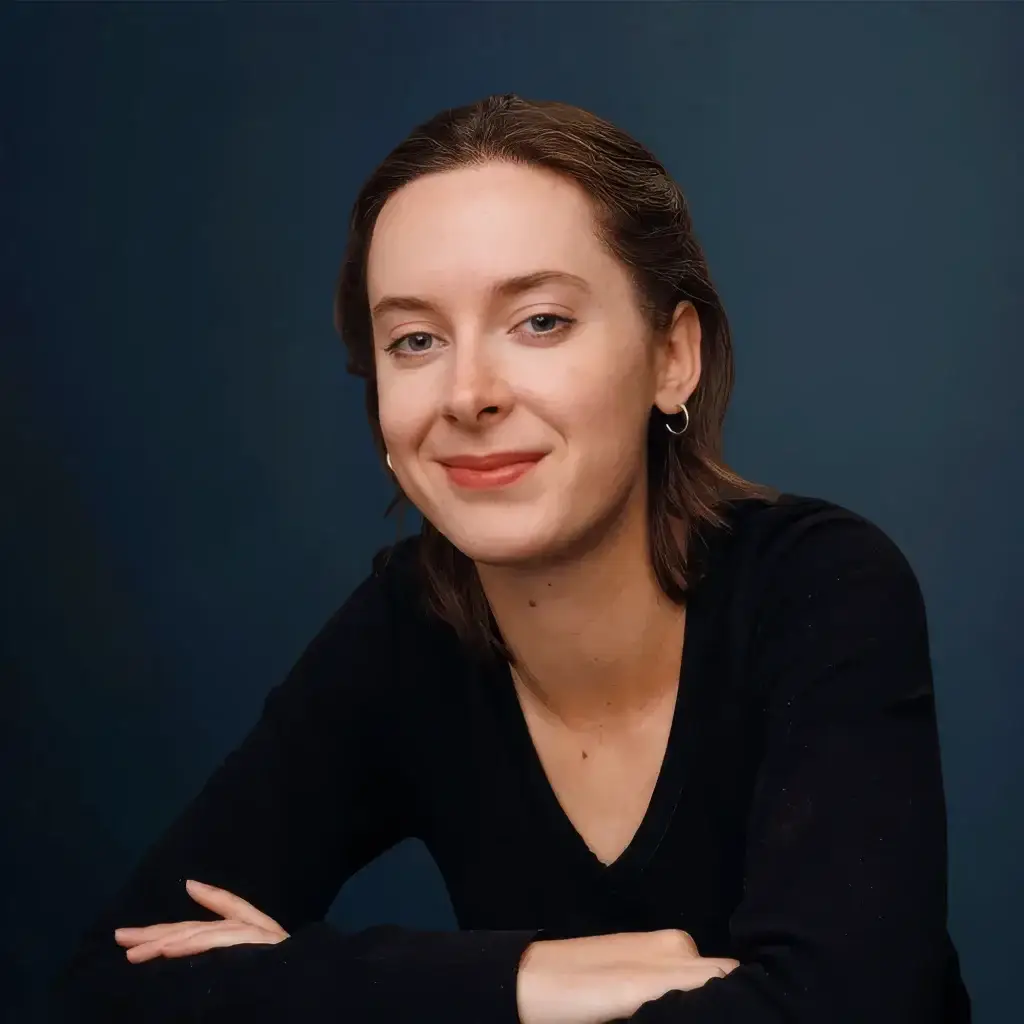 Smiling woman with brown hair wearing a black shirt against a blue background.