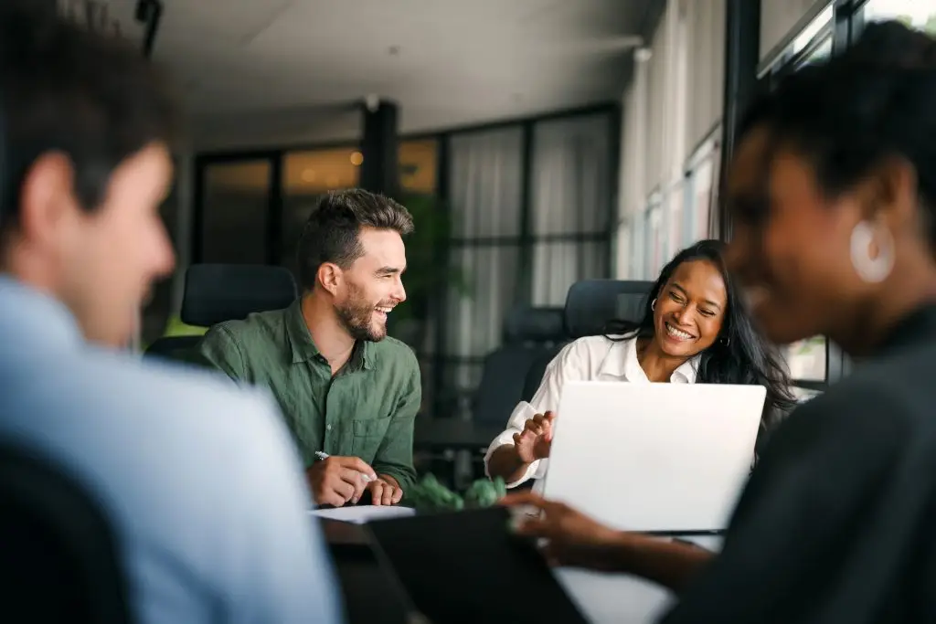 Four colleagues smiling during a business meeting in a modern office setting, engaged in teamwork and discussion.