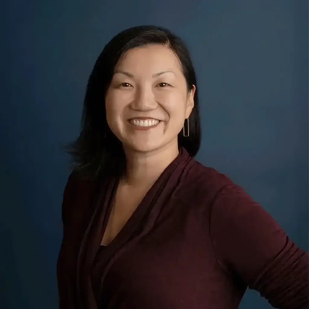 Smiling person in a burgundy top against a blue background, posing confidently.