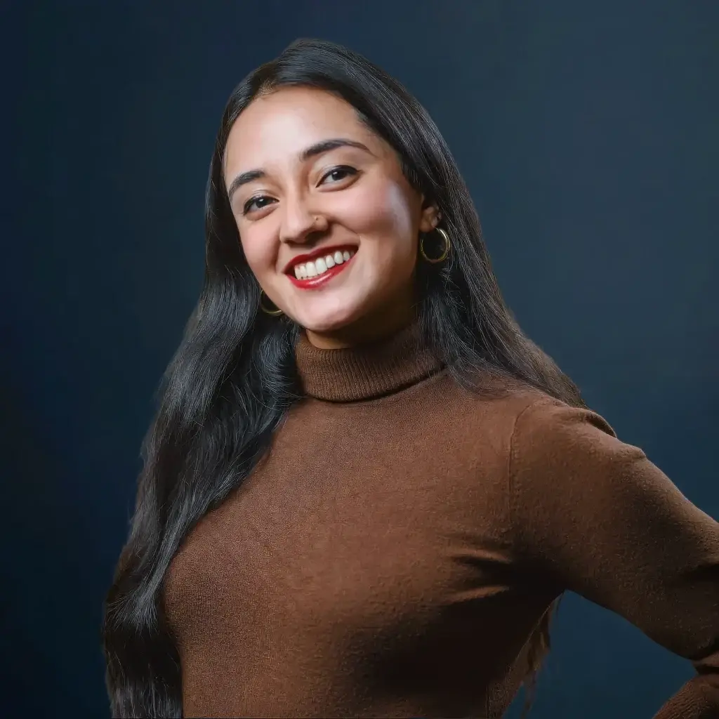 Smiling woman in brown turtleneck sweater against dark blue background.
