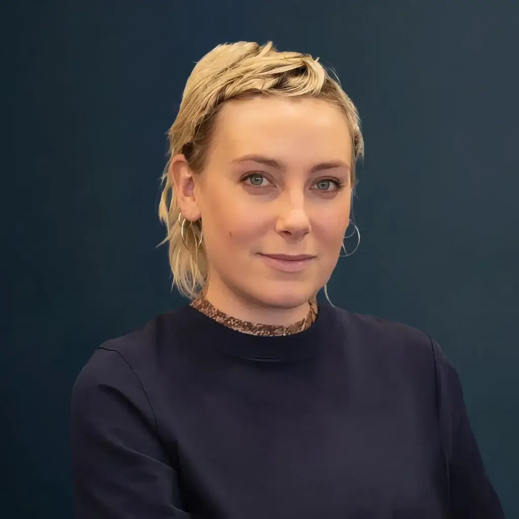 Portrait of a confident person in a dark shirt against a blue background.