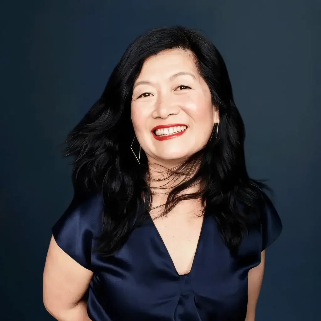 Smiling woman with long dark hair and navy blouse against dark blue background.