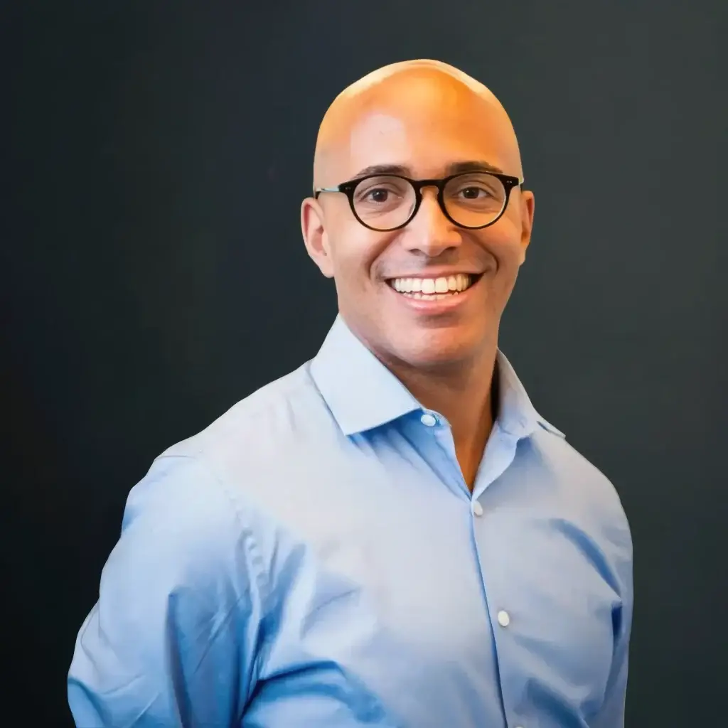 Smiling person in glasses with a blue shirt against a dark background.