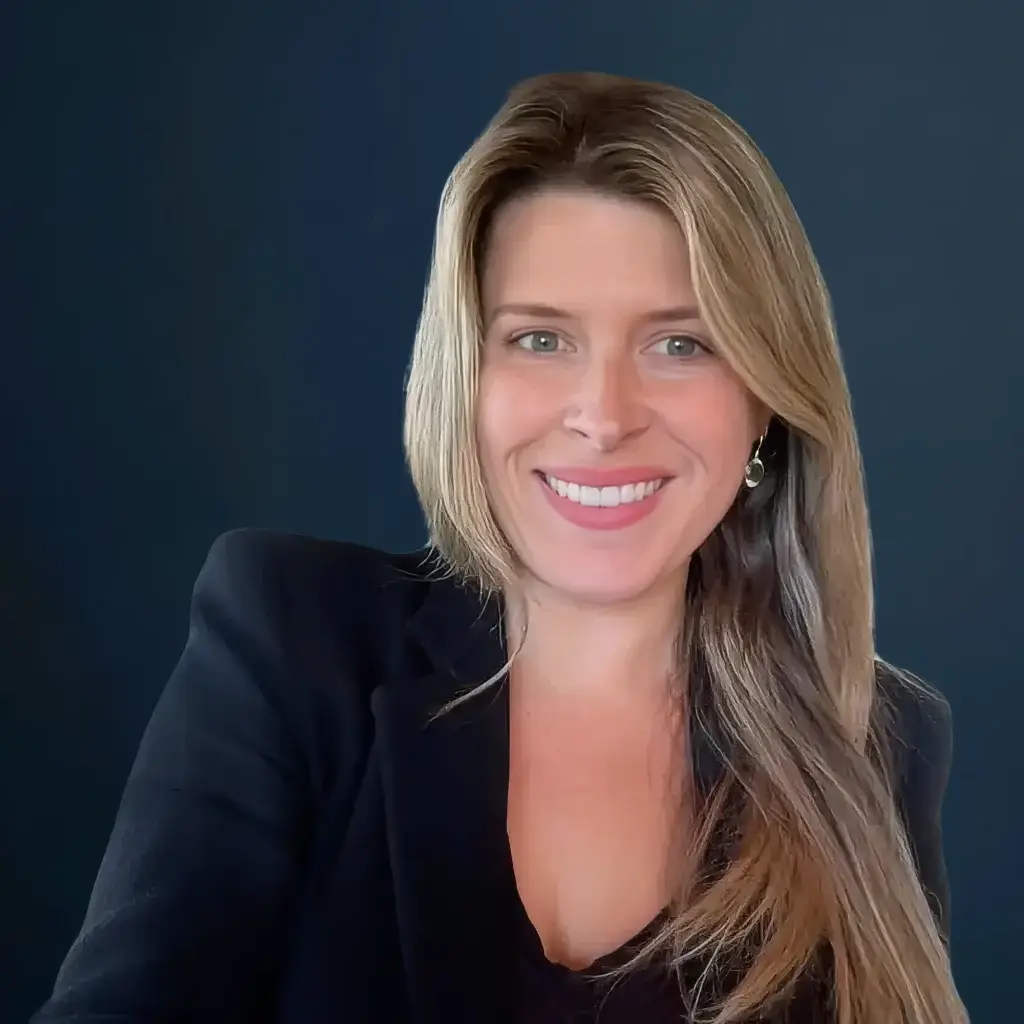 Smiling woman in black blazer, professional headshot against dark background.