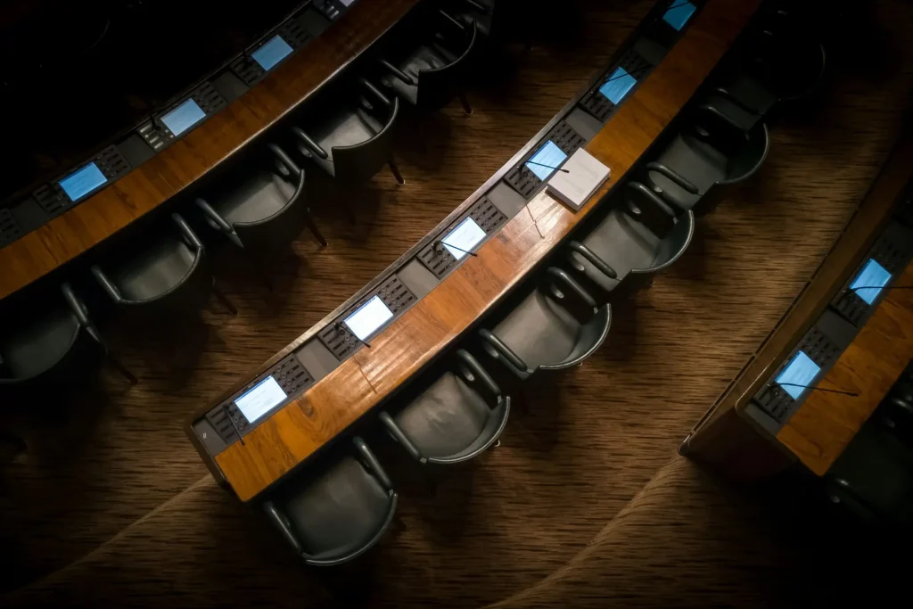 Conference room with wooden desks and empty chairs, ready for a meeting.